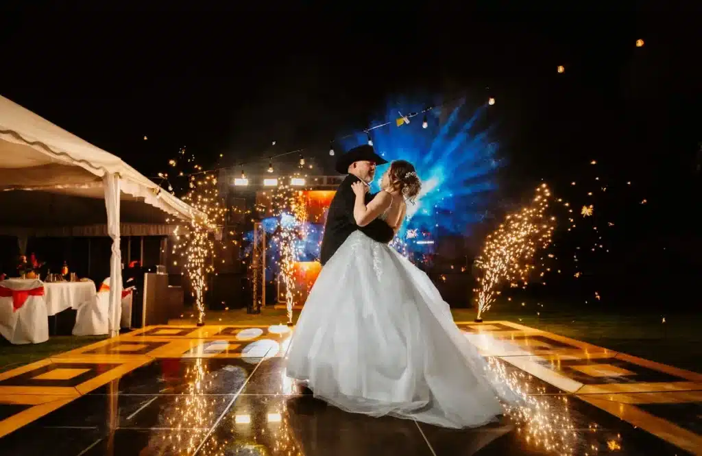 Femme en robe claire tenant un sac à main bordeaux lors d'une célébration en soirée avec feux d'artifice