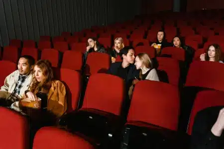 Foule de spectateurs dans le hall d'un cinéma illuminé, tenant des tickets et du popcorn