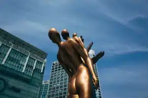 Statue en bronze noir dans une place parisienne avec des visiteurs qui la touchent