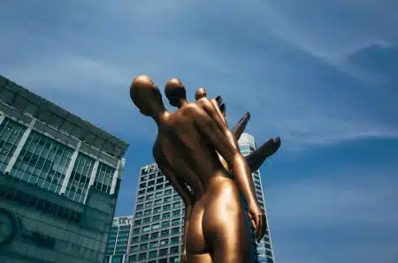 Statue en bronze noir dans une place parisienne avec des visiteurs qui la touchent