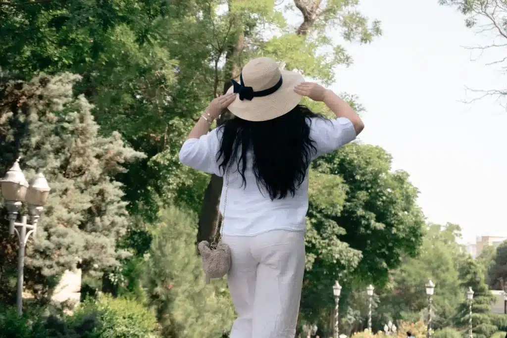 Femme vêtue d'un pantalon lin blanc fluide et d'une blouse légère, accessoirisée d'une fine ceinture, dans un cadre urba