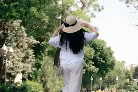 Femme vêtue d'un pantalon lin blanc fluide et d'une blouse légère, accessoirisée d'une fine ceinture, dans un cadre urba