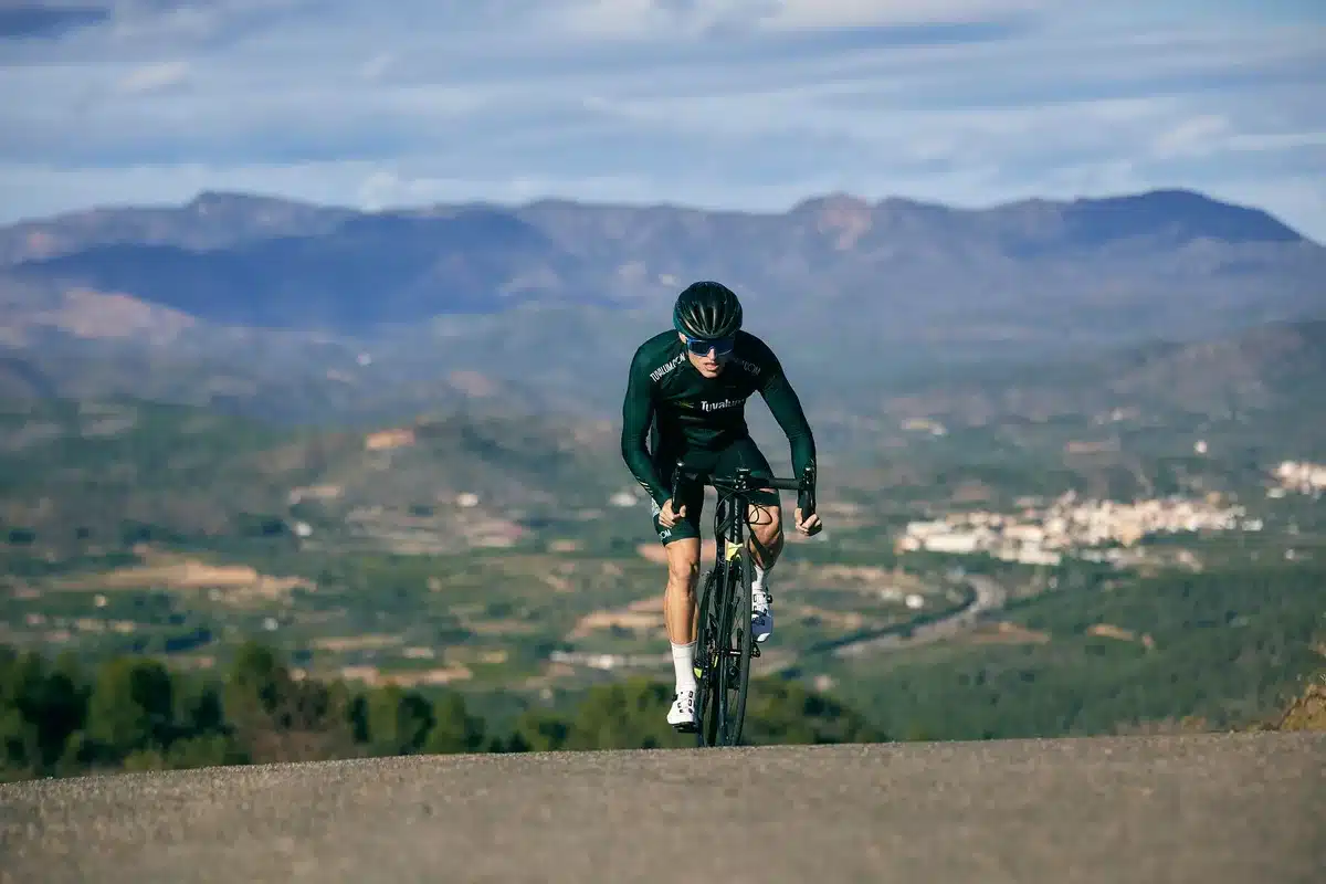 Cycliste grimpeuse en montée sur route de montagne, paysage alpin en arrière-plan