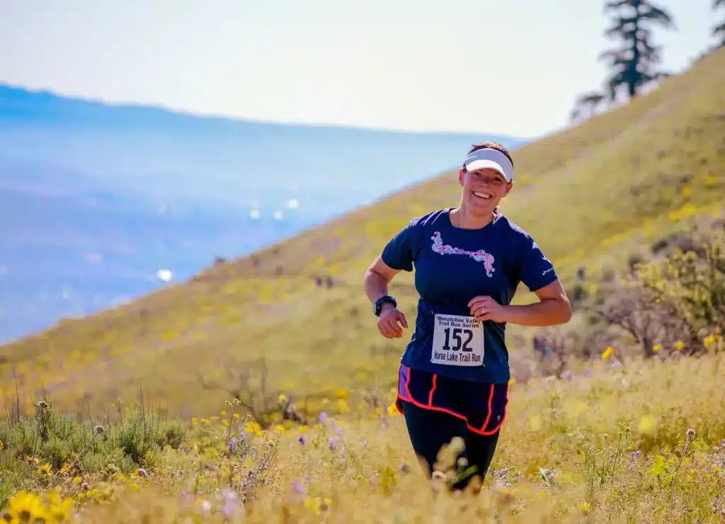 Coureurs de trail en montée raide sur un sentier alpin en plein jour, paysage rocheux et pics enneigés en arrière-plan