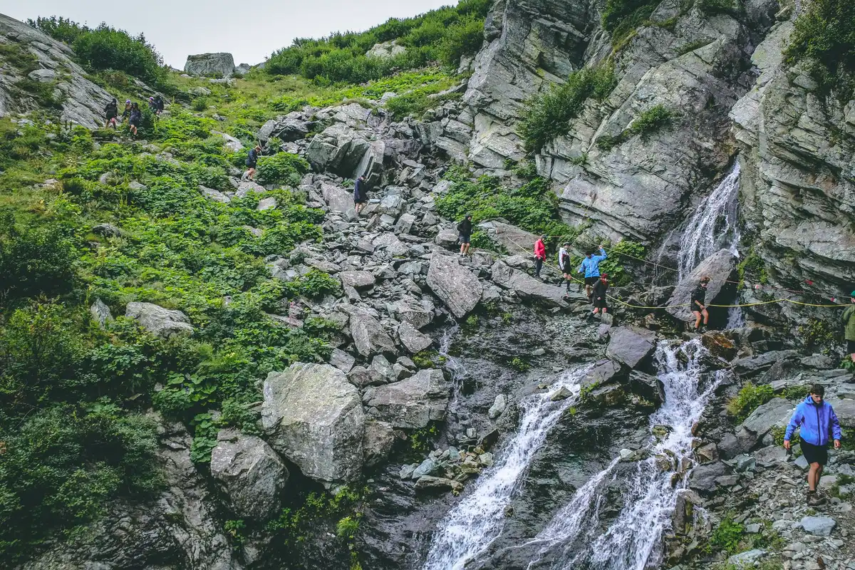 Équipe de coureurs en trail naviguant sur un terrain alpin sauvage sans balisage continu.