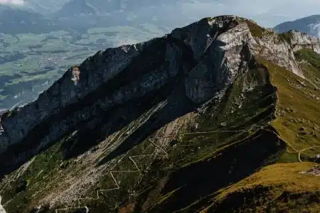 Coureur en trail montant une crête alpine escarpée au lever du jour, avec les montagnes en arrière-plan.