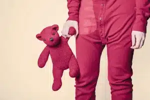 Un ours en peluche et un sac d'enfant sur un banc d'école, aire de jeux en arrière-plan