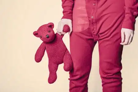 Un ours en peluche et un sac d'enfant sur un banc d'école, aire de jeux en arrière-plan
