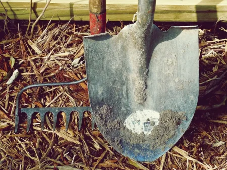 Chaussures de travail près d'outils sur une terrasse ensoleillée, herbe humide en arrière-plan