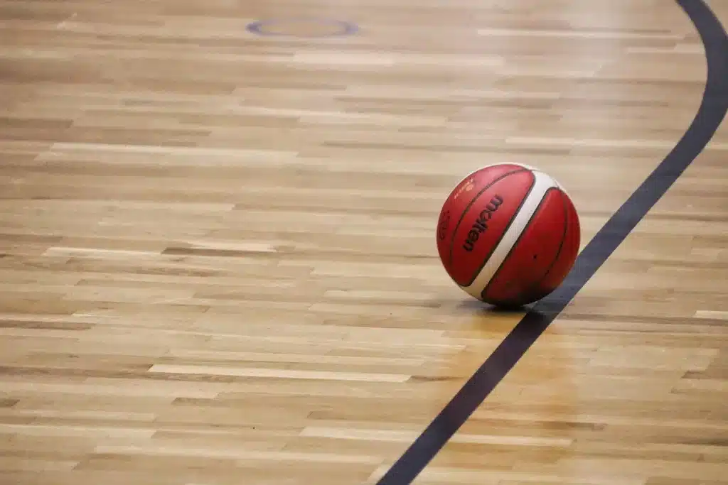 Mains tenant un ballon de basket sur un banc dans un gymnase en plein jour