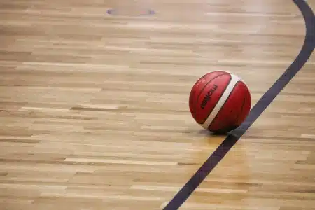 Mains tenant un ballon de basket sur un banc dans un gymnase en plein jour