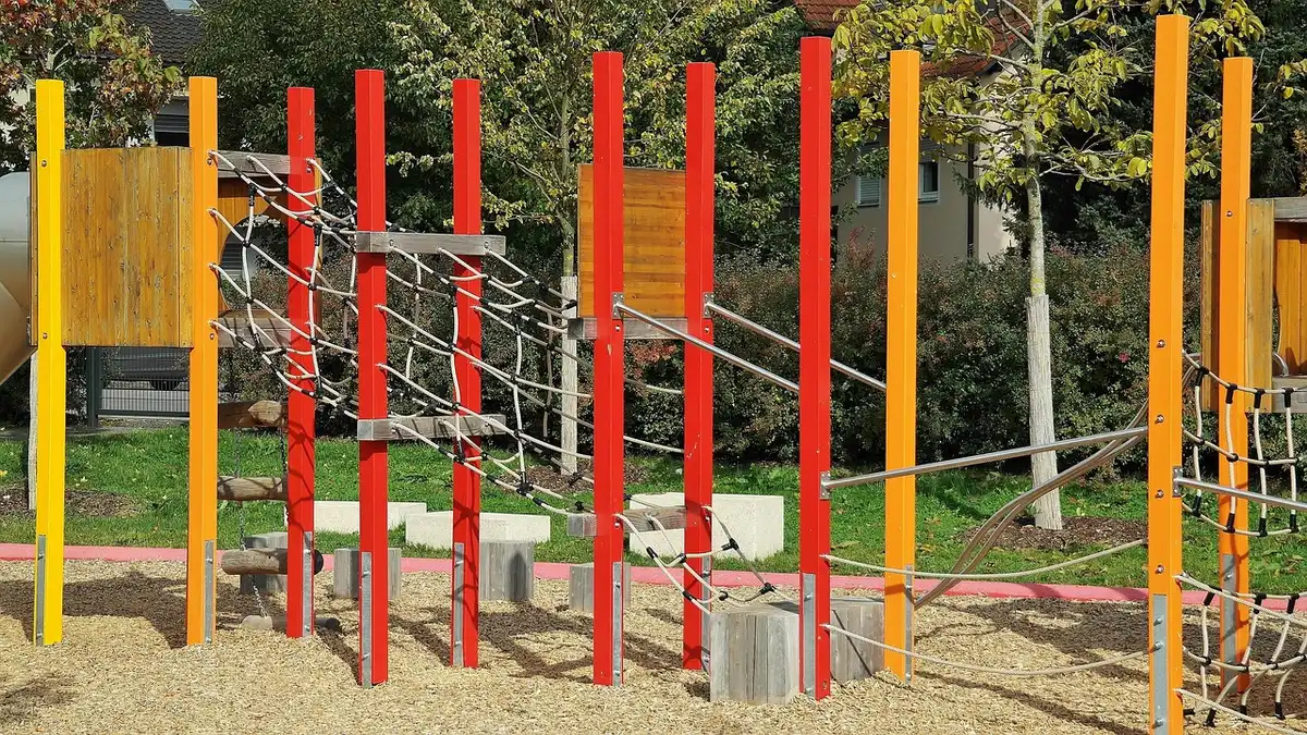 Jeux en bois taille XXL installés sur pelouse, enfants jouant au loin