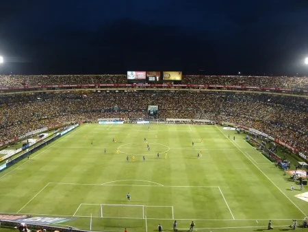 Spectateurs dans un stade en plein jour, mains sur la rambarde et tribunes en arrière-plan